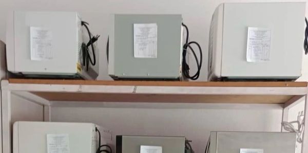 Six microwave ovens arranged on two shelves against a wall.