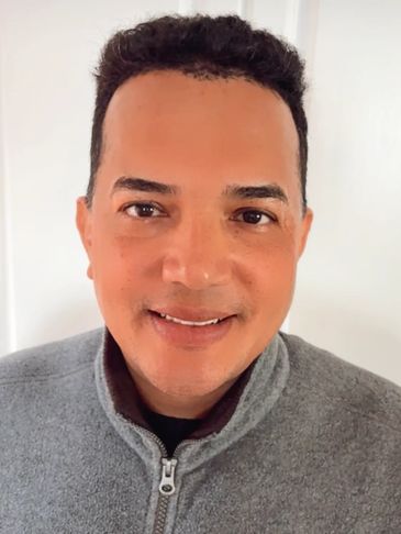 Smiling man wearing a gray zip-up sweater.