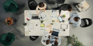 Five people collaborating around a white table with laptops and documents.
