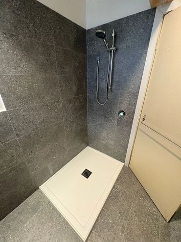 Minimalist shower area with gray tiles and white shower base.