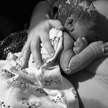 Un nouveau-né couvert de vernix tient la main d'un adulte.