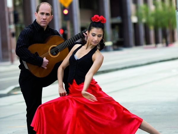 A flamenco dancer in a red dress with a guitarist performing on the street.