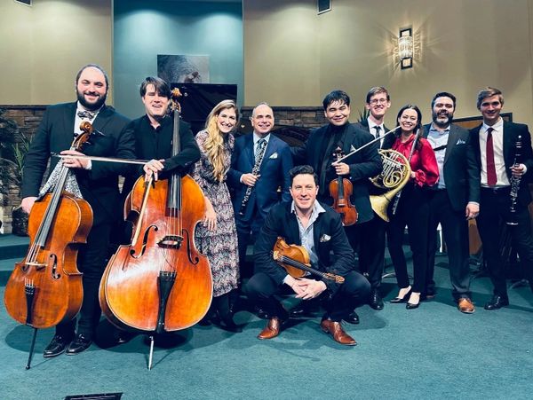 A group of nine musicians posing with their instruments on stage.