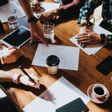 People collaborating around a table with documents, tablets, and coffee cups.
