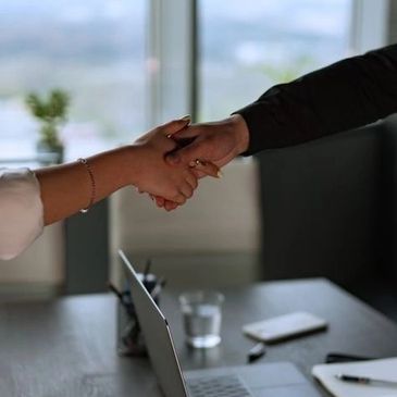 Two people shaking hands over a laptop in an office setting.