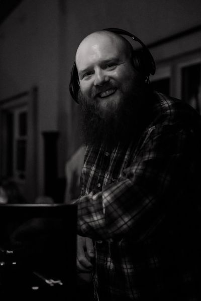 Bearded man smiling wearing headphones in black and white photo.