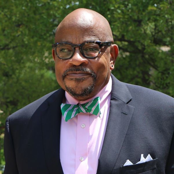 Man in glasses wearing a suit and green striped bow tie outdoors.