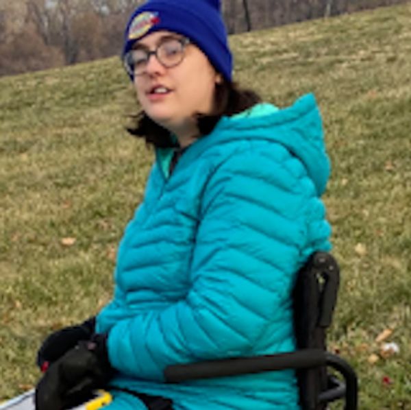 Young lady wearing glasses, a blue stocking cap, and a green coat.