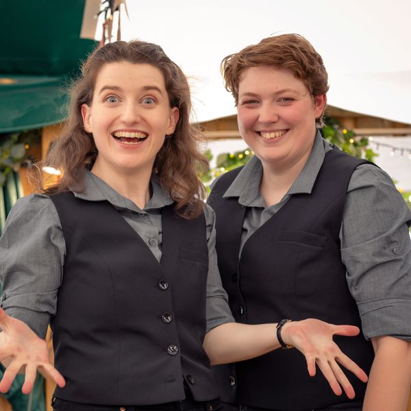 Two women stand shoulder to shoulder. Both are smiling. Myth-Fits, 2022 Photo by Kristian Lawrence.