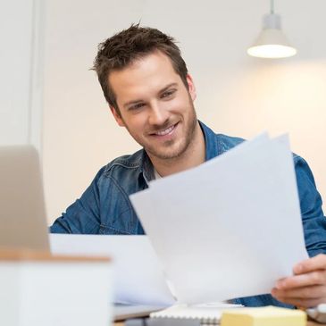 A young male person is holding a document and smiling.