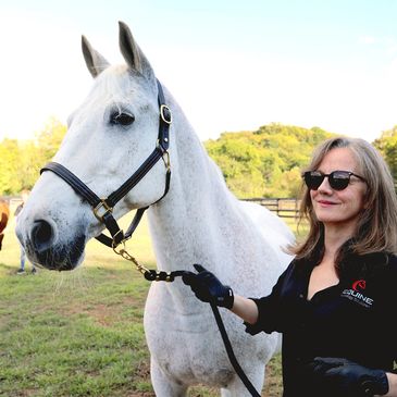 Woman with sunglasses holding a white horse in a sunny outdoor setting.