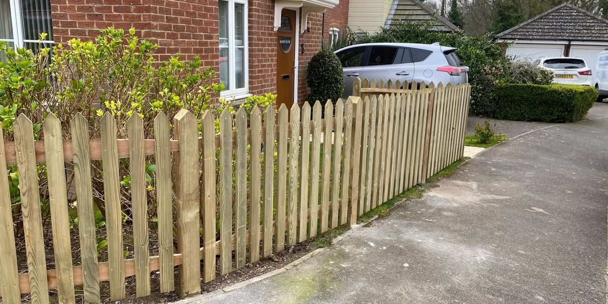 Wooden picket fence along a driveway and house entrance.