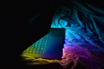 Image of half open laptop with rainbow glow on fabric. Suggestive of online sessions.