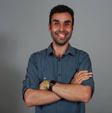 Smiling man with folded arms wearing a striped shirt against a gray background.