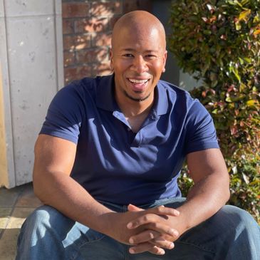 Smiling man in navy blue polo shirt sitting outdoors on a sunny day.