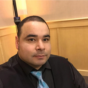 Man with short hair wearing a black shirt and blue patterned tie.