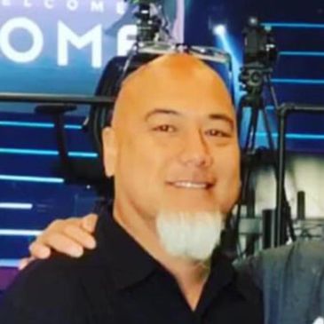 Smiling bald man with a white goatee in a black shirt.