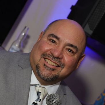 Smiling man in a gray suit holding a microphone.