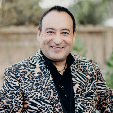 Man wearing a leopard print jacket holding a microphone and smiling.