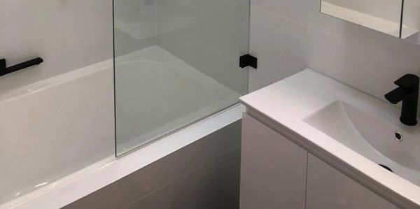 Modern bathroom with white bathtub, glass partition, and black fixtures.