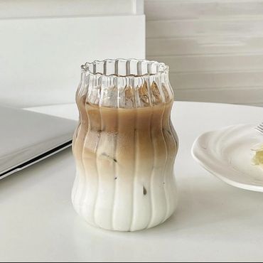 Aesthetic iced latte in a uniquely shaped glass on a white table.