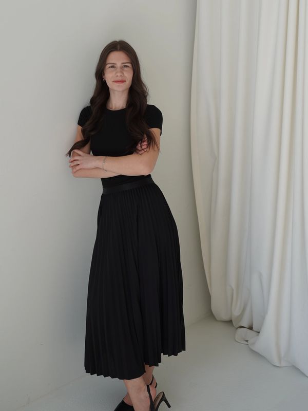 Woman in black dress standing against wall.