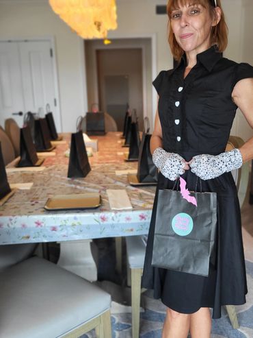 Woman in black dress holding a party bag in a decorated dining room.