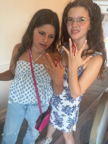 Two girls showing fake bloody wounds on their fingers, one making a playful face.