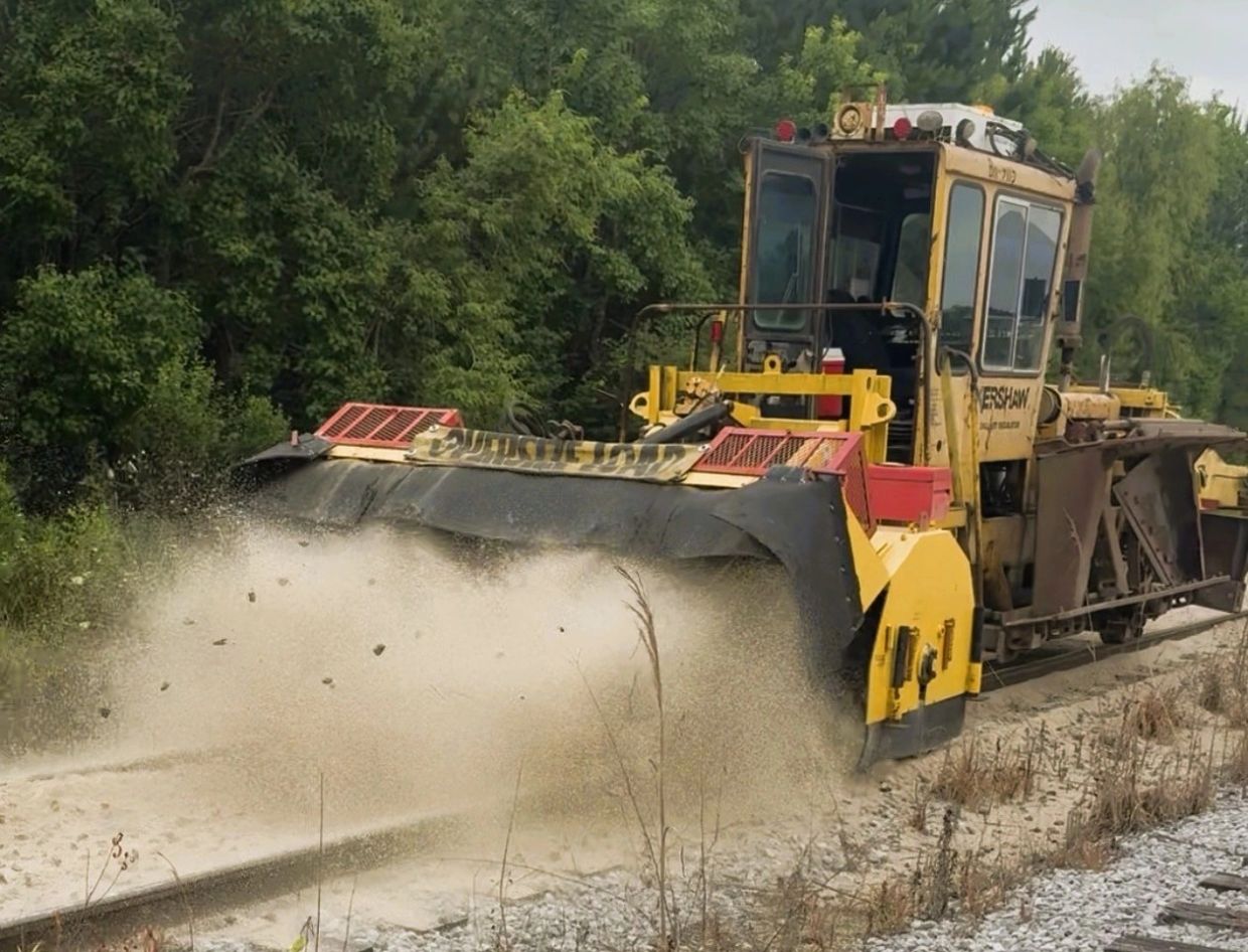 Yellow railroad maintenance machine spreading gravel on tracks.