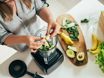 Woman standing at kitchen counter with fresh fruit and making a smoothie