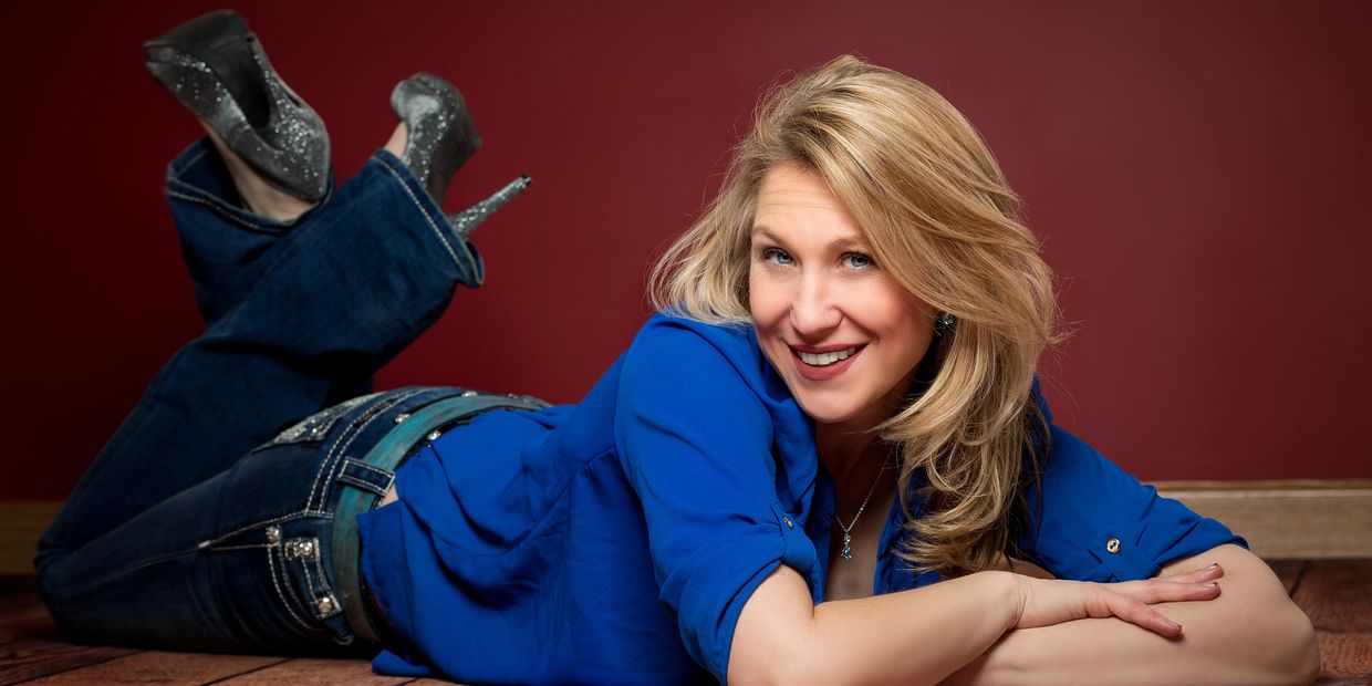 Blonde female in a blue shirt and jeans with a maroon background.