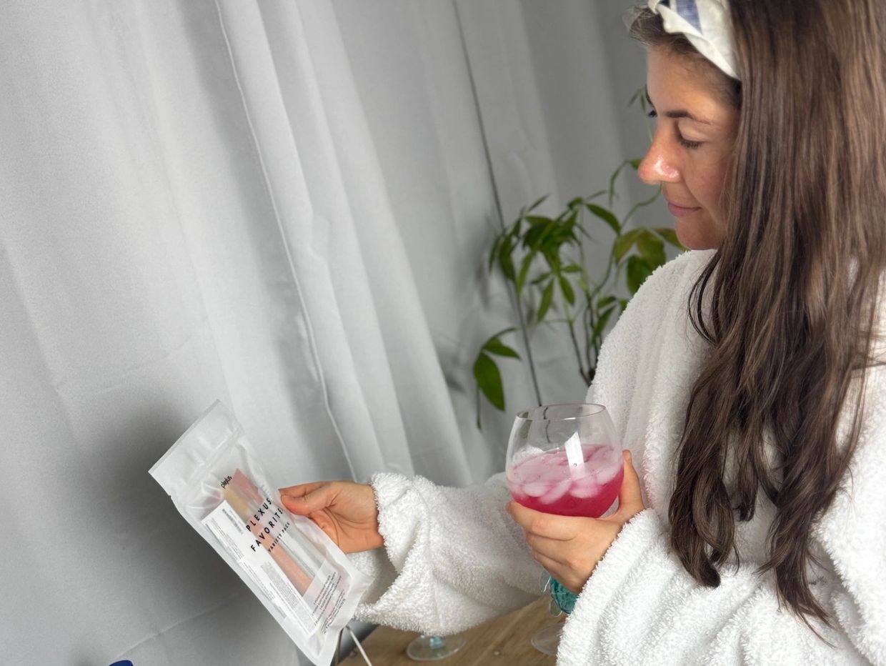 Woman in white robe holding a pink drink and a packet.