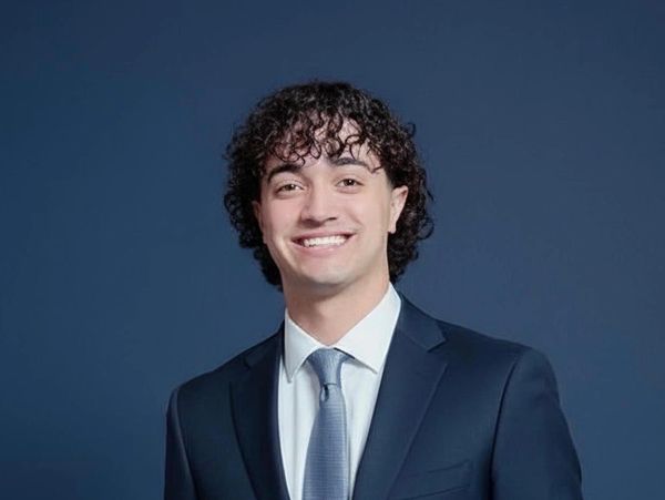 Young man in a navy suit smiling confidently against a blue background.