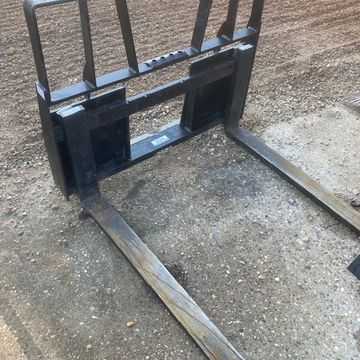 Heavy-duty forklift attachment with long metal forks on gravel ground.