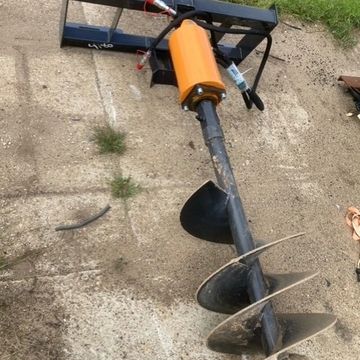 Large ground auger tool with an orange motor attachment on concrete.