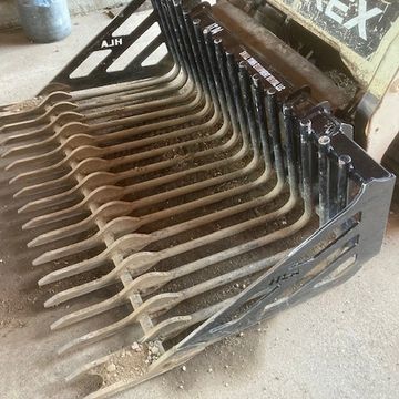 Heavy-duty skid steer attachment with multiple metal tines for sifting or raking.