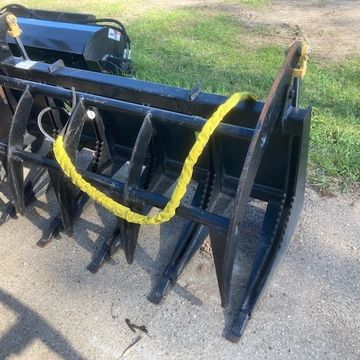 A black metal grapple attachment for heavy machinery on a concrete surface.
