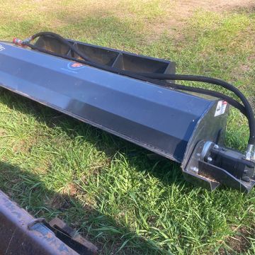 A large black industrial attachment with hydraulic hoses on grass.