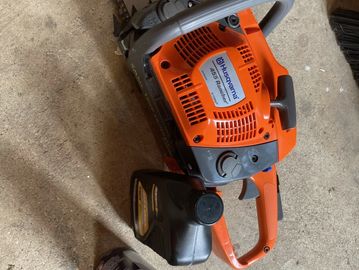 A Husqvarna chainsaw with fuel and oil cans on a concrete floor.