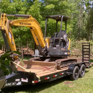 A New Holland mini excavator on a trailer in a grassy area.