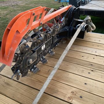 A trencher attachment secured on a wooden trailer bed.