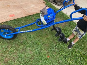 A child holding a blue earth auger on grass.