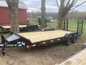 Black flatbed trailer with wooden deck parked outdoors near trees and a red barn.