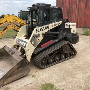 A Terex skid steer loader parked on concrete near a barn.