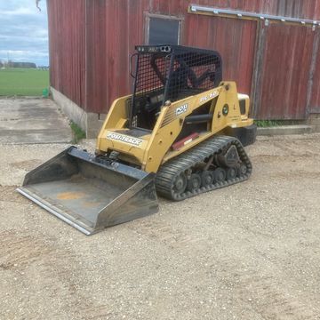 Yellow Posi-Track RC-60 skid steer loader parked by a red barn.