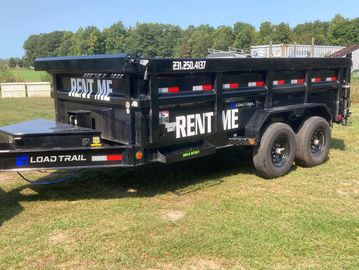 Black Load Trail trailer with RENT ME signs, parked on grass.