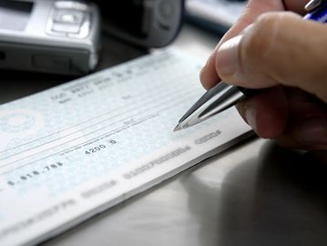 A hand writing on a check with a pen.