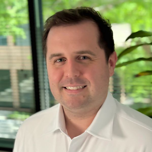 Smiling man in a white shirt with a green outdoor background.