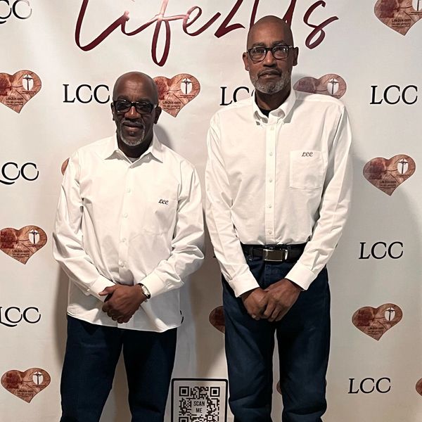 Two men in white shirts standing in front of a Life2Us backdrop.