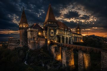 Illuminated medieval castle at dusk under a dramatic sky.